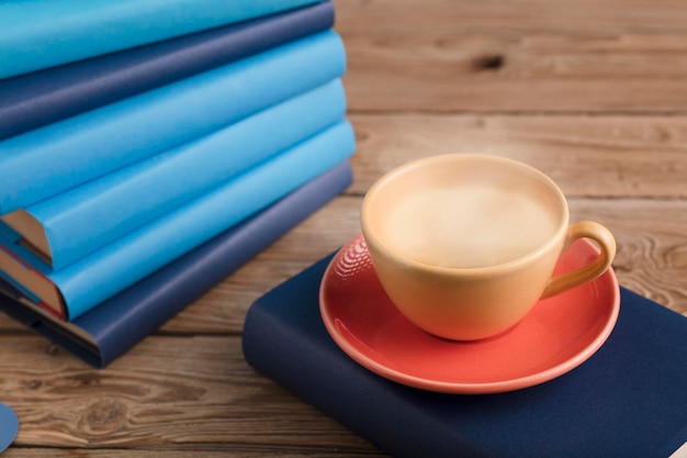 Tasse de café jaune avec de la vapeur chaude de lait sur un livre avec des livres bleu clair et un fond en bois