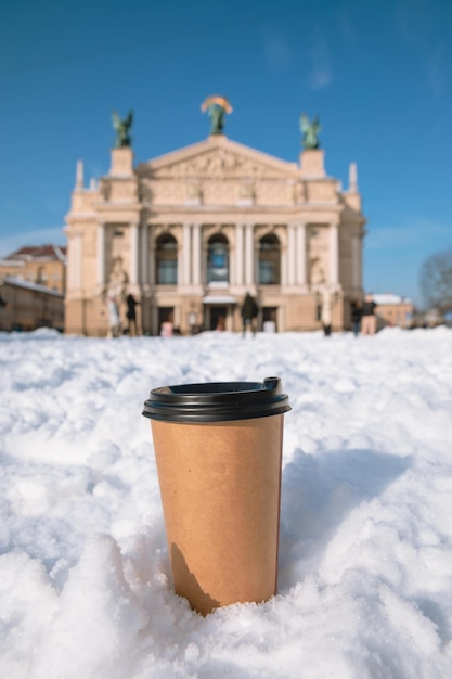 Tasse à café jetable dans la neige lviv city opera building sur fond