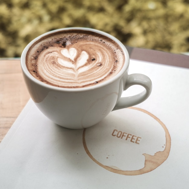 Une tasse de café latte art avec coeur dans une tasse blanche sur un livre de café