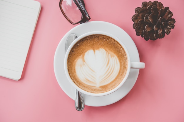 Photo tasse de café latte art forme de coeur avec des outils de bureau sur la table rose