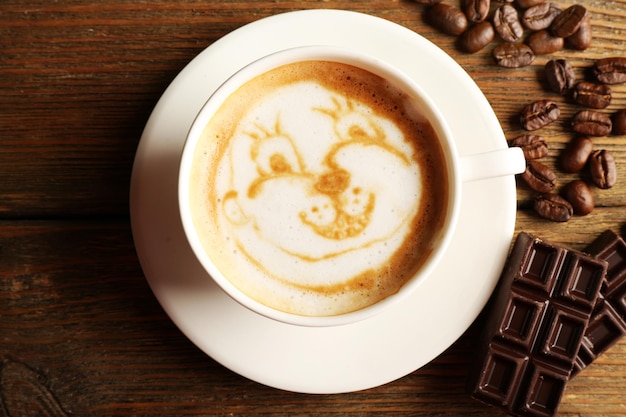 Tasse de café latte art avec grains et chocolat sur la vue de dessus de table en bois