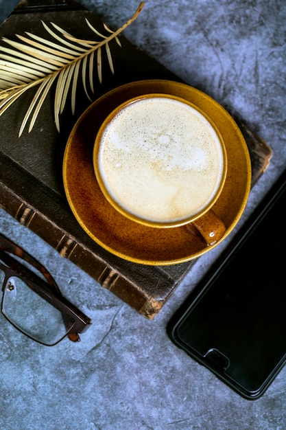 Une tasse de café sur un livre, des lunettes et une vue de dessus de téléphone.