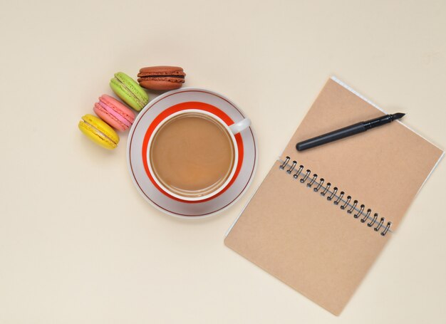 Tasse de café, macarons colorés, bloc-notes avec stylo sur fond.