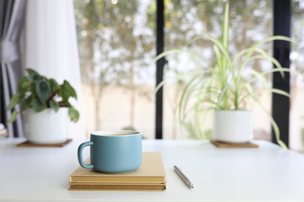 Tasse à café mat moderne bleu et crayon et cahier marron sur table blanche avec pot de plantes et clavier