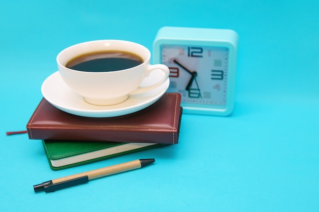une tasse de café, une montre et un cahier sur fond bleu. le concept du thème de l'entreprise.