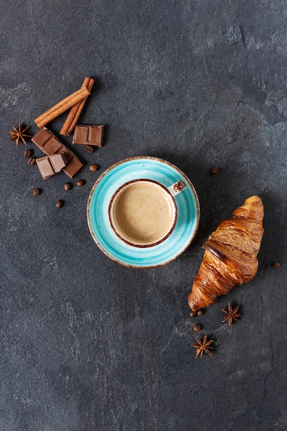 Tasse de café avec des morceaux de chocolat aux épices de cannelle et d'anis et un croissant sur fond noir