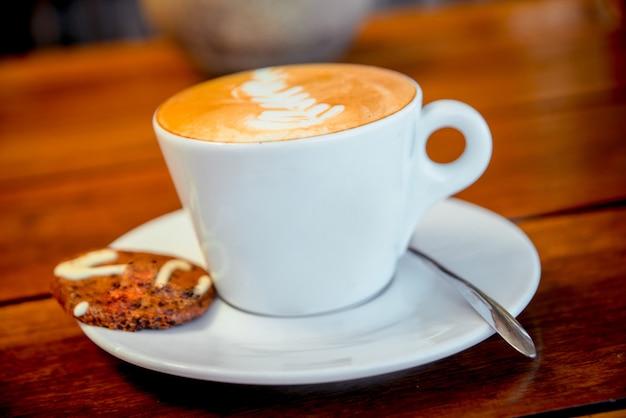 Tasse de café avec mousse et biscuits sur la table.