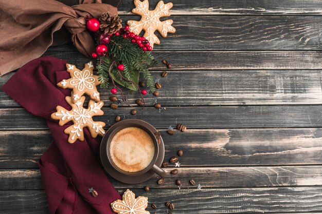 Une tasse de café avec de la mousse sur un bois sombre avec du pain d'épice sous forme de flocons de neige.