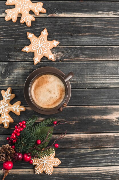 Une tasse de café avec de la mousse sur un bois sombre avec du pain d'épice sous forme de flocons de neige.