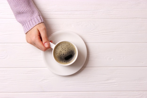 Tasse de café avec mousseux dans les mains des femmes sur la vue de dessus de table en bois