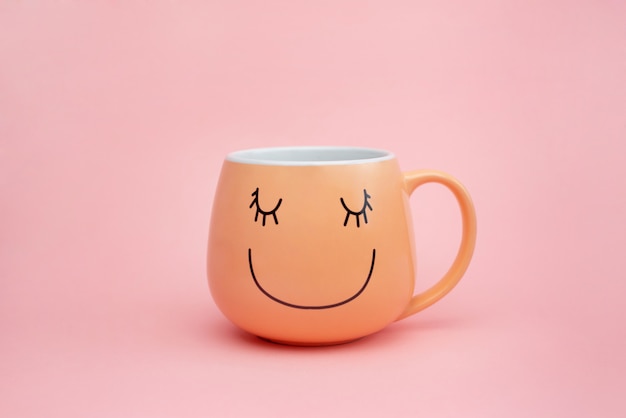 Tasse de café sur le mur rose avec un sourire heureux sur la tasse.