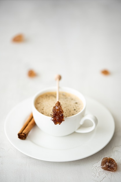 Une tasse de café noir avec de la cannelle et du sucre caramélisé sur un bâton, sur un tableau blanc