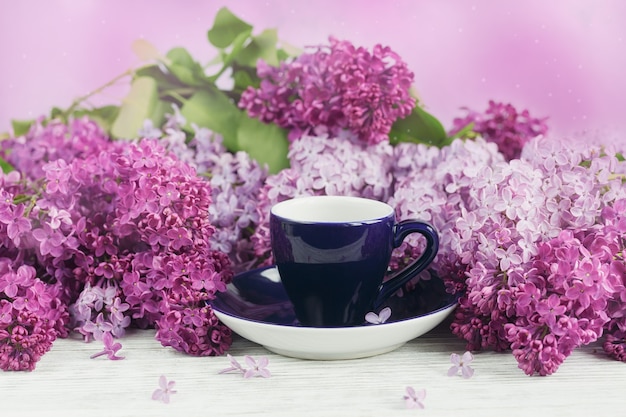 Tasse de café noir, fleurs lilas et macarons français pastel sur table en bois clair