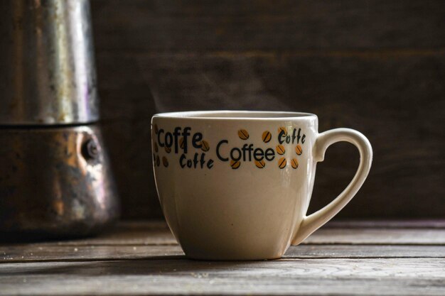 Une tasse de café noir et un geyser sur une table en bois.