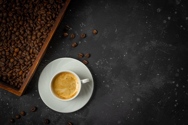 Photo tasse de café noir et grains de café torréfiés dans une boîte en bois sur un fond gris foncé