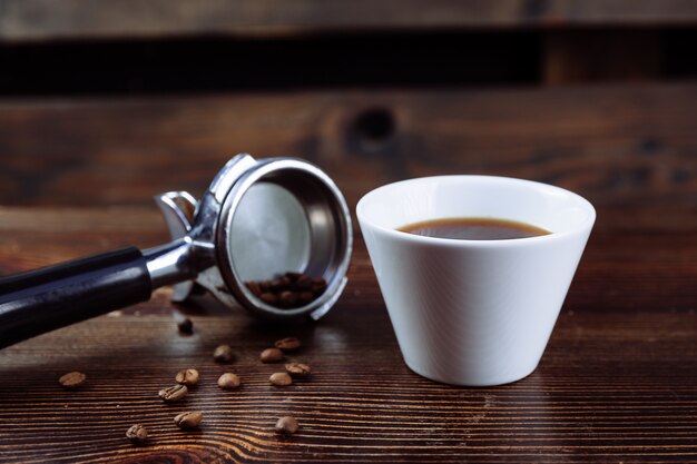 Une tasse de café noir, des grains de café torréfiés et un support de machine à expresso sur fond sombre.