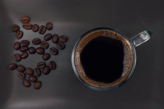 Tasse de café noir sur une plaque brune avec des grains de café