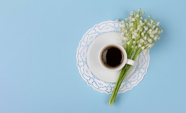 Tasse de café noir sur une soucoupe et un bouquet de fleurs de muguet