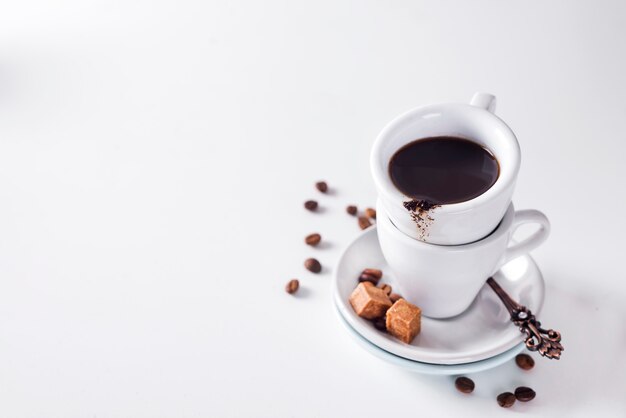 Tasse de café noir sur une soucoupe avec du sucre brun sur un fond blanc