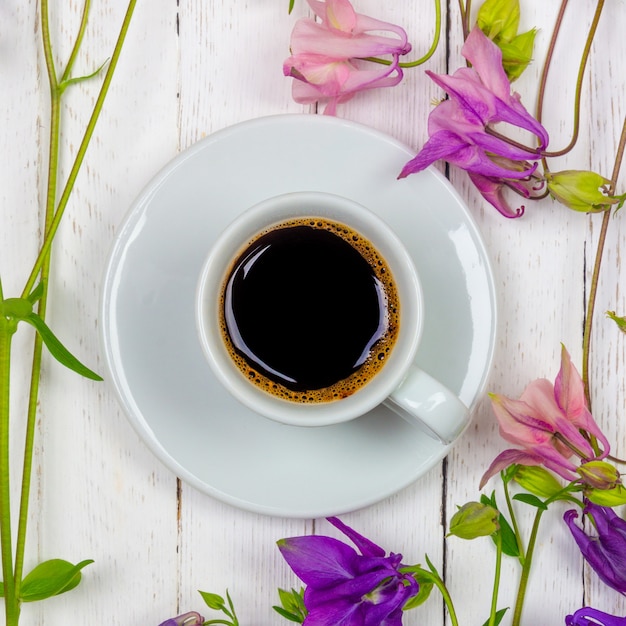 Une tasse de café noir sur une soucoupe et des fleurs sur une table blanche