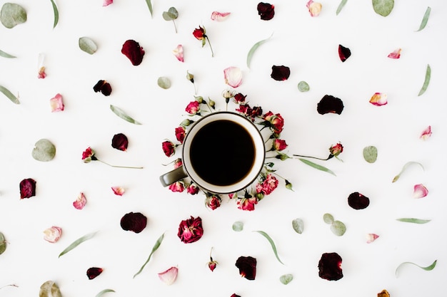 Tasse à café noire et bouquet de boutons de roses rouges à l'eucalyptus sur blanc