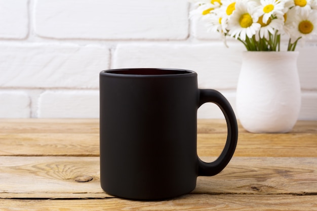 Tasse à café noire avec bouquet de camomille dans un vase rustique