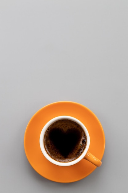 Tasse de café orange avec mousse de coeurisoléVue de dessusPlace pour le texteFormat vertical