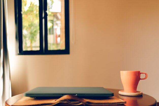 Tasse à café orange et ordinateur portable sur la table dans le café.