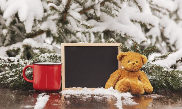 Tasse de café, ours en peluche et tableau noir sur table en bois dans la neige