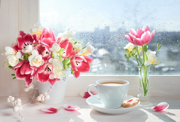 Tasse de café sur le panneau de la fenêtre, soleil après la pluie avec des fleurs de printemps