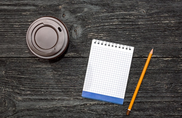 Tasse de café en papier et bloc-notes avec un crayon sur une table en bois