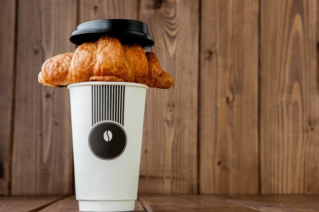 Tasse à café en papier et croissants sur fond en bois, espace copie.