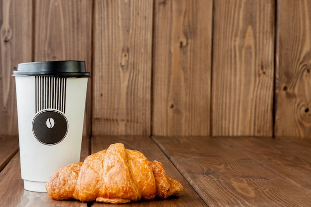 Tasse à café en papier et des croissants sur fond en bois