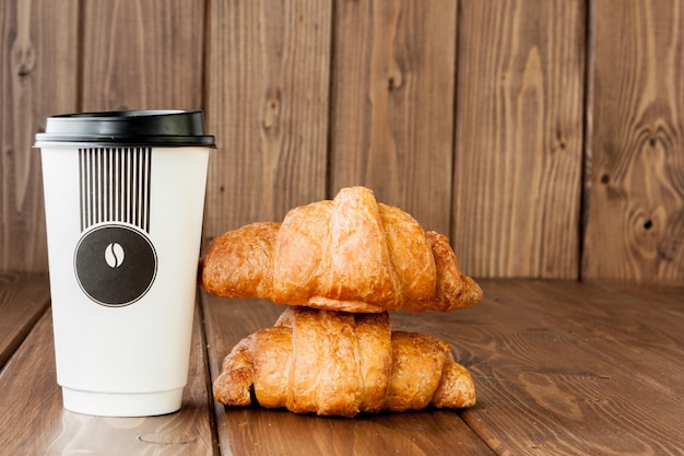 Tasse à café en papier et des croissants sur fond en bois