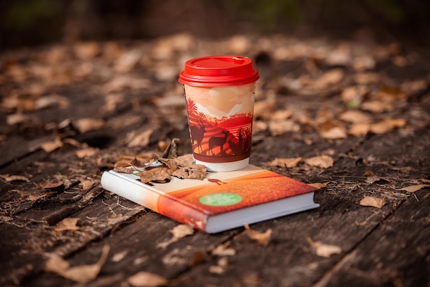 une tasse de café en papier et un livre sur une table en bois parmi les feuilles tombées