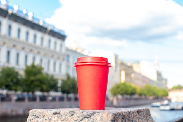 Tasse de café en papier rouge sur la balustrade sur le quai de la rivière