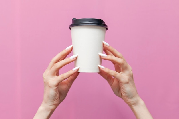 Tasse de café en papier vierge blanche dans les mains d'une femme sur fond isolé rose