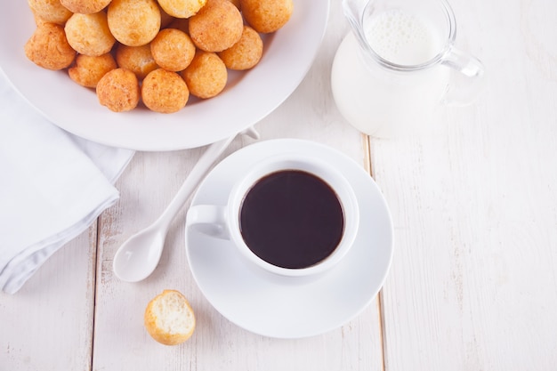 Tasse de café avec des petites boules de beignets de fromage blanc fait maison dans une assiette