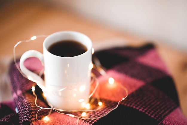 Tasse de café sur une pile de pulls avec des lumières de Noël se bouchent. L'hiver.