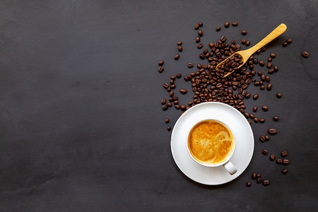 Tasse de café sur un plancher en bois noir avec des grains de café et une cuillère en bois