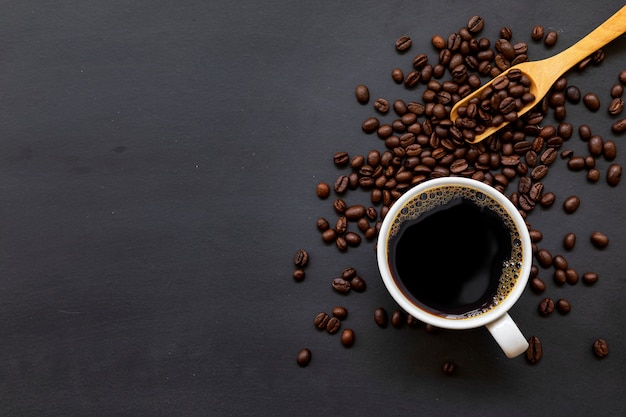 Tasse de café sur un plancher en bois noir avec des grains de café et une cuillère en bois