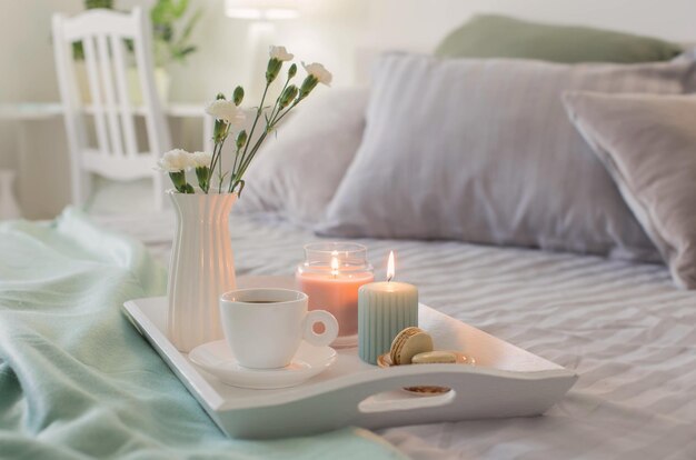 Tasse de café sur un plateau en bois sur le lit avec des fleurs et des bougies