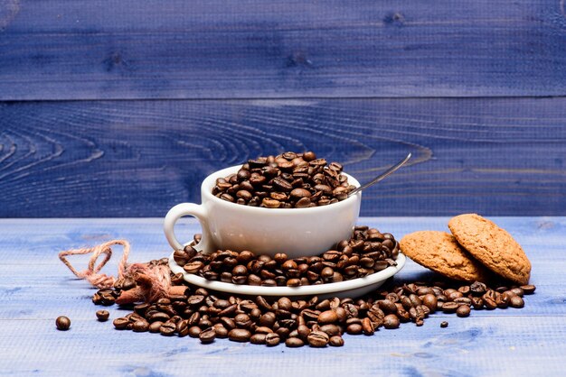 Tasse à café pleine de haricots torréfiés bruns bleu fond en bois Menu de boissons au café Pause-café avec biscuit à l'avoine Grains de café torréfiés frais Concept de caféine Boisson pour l'inspiration et la charge énergétique