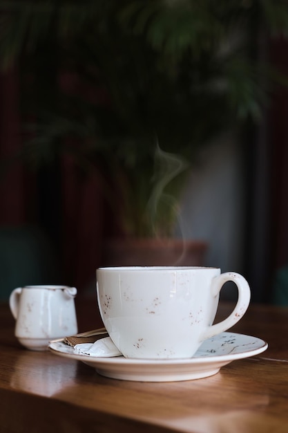 Une tasse de café et un pot à lait sur une table dans un vieux café Photo en vapeur de couleur vintage s'élevant du cadre vertical du café mise au point sélective Idée pour économiseur d'écran ou article de menu sur le café