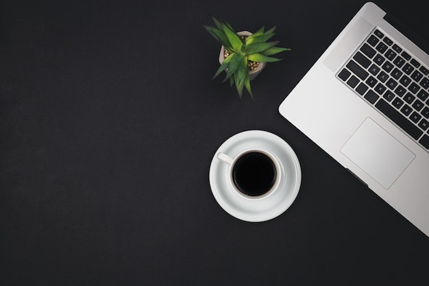Tasse à café pour ordinateur portable et plante de bureau sur la vue de dessus de fond noir