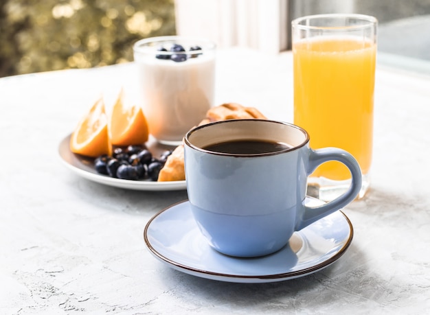 Tasse de café pour le petit déjeuner avec jus, orange, myrtille et yaourt sur béton