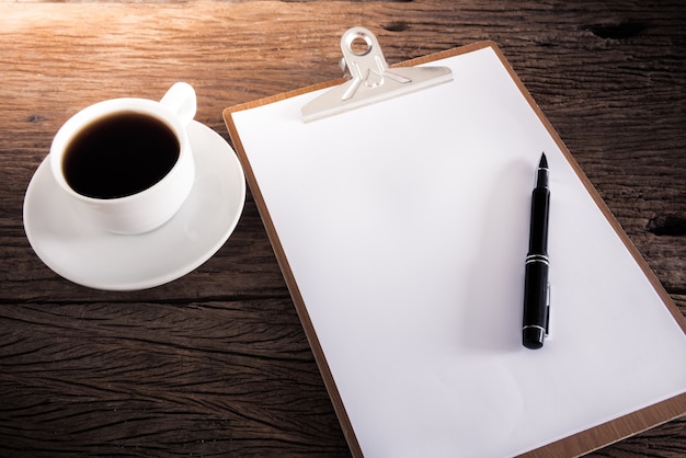 tasse de café et presse-papiers avec une page blanche et un stylo sur la table en bois