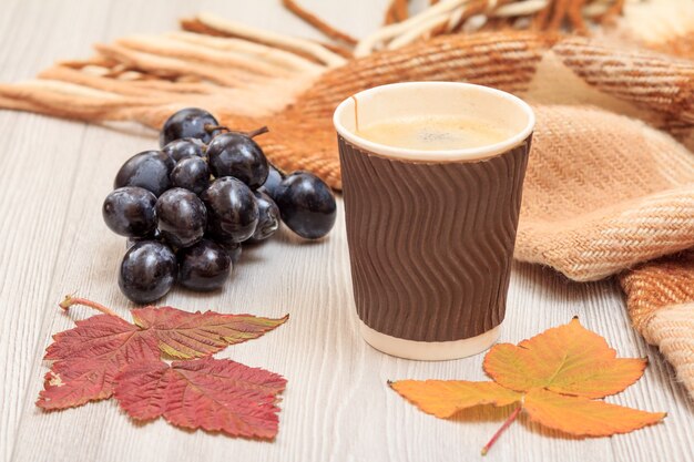 Tasse de café, raisins, plaid à carreaux et feuilles sèches sur planches de bois. Une nature morte d'automne.