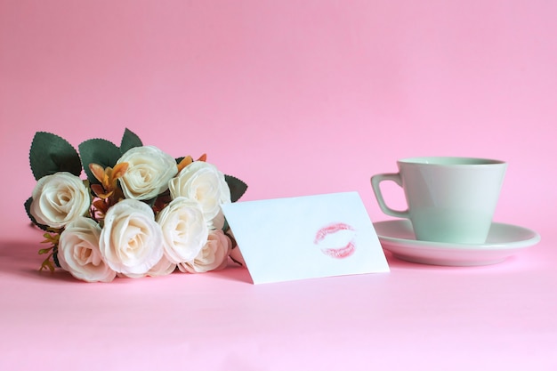 Tasse de café à la rose et baiser sur une enveloppe blanche isolée sur fond rose