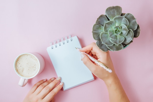 Tasse à café rose du matin, cahier propre, stylo et fleur en pot sur fond rose